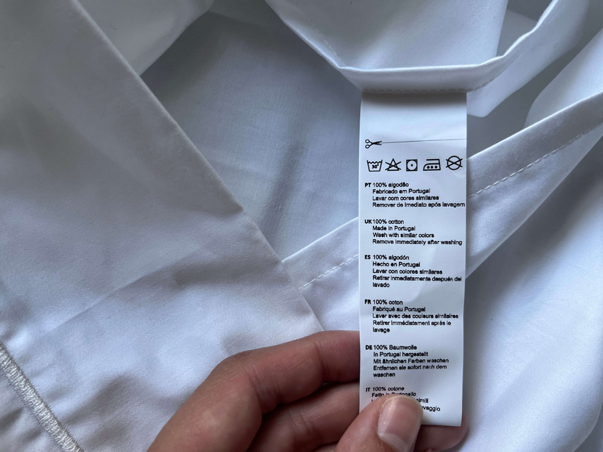 Mão a segurar na etiqueta de uma fronha de almofada para mostrar que o material é 100% algodão